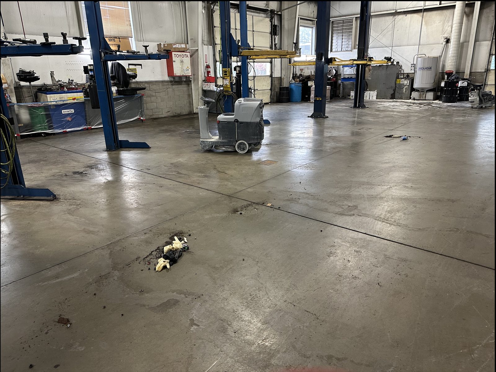 Dealership shop concrete floor before clean and seal work, showing stains and wear from daily use.